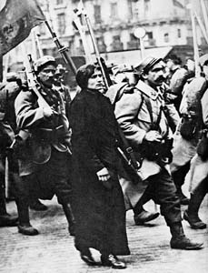 La femme d’un soldat mobilisé marche à ses côtés alors que son régiment  part au front. Malgré les drapeaux et sans doute la liesse populaire, on ne lit aucun enthousiasme sur les visages… Paris, 1er août 1914.
 