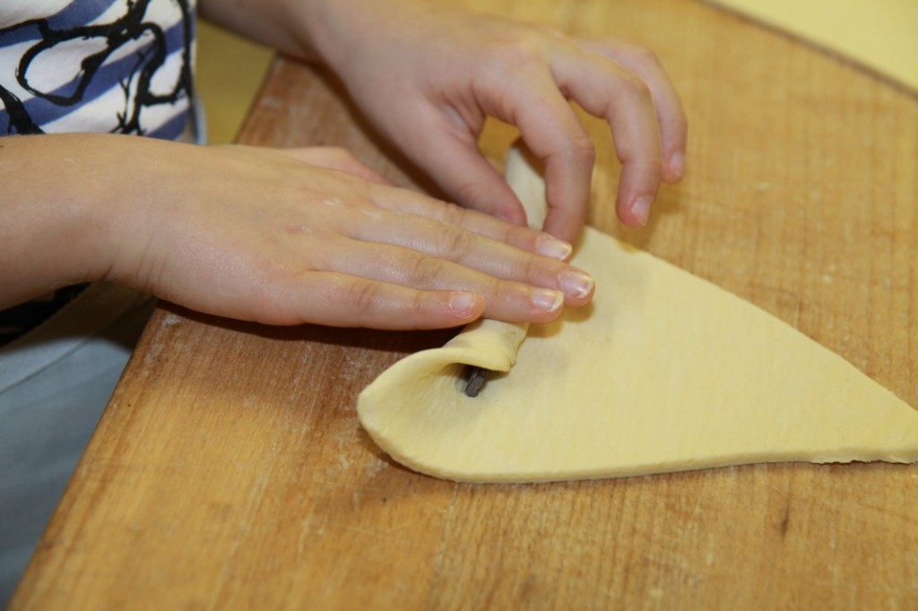 CroissantzubereitungSie rollt den Teig mit der Schokoladenstange auf.