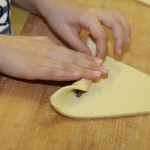 CroissantzubereitungSie rollt den Teig mit der Schokoladenstange auf.